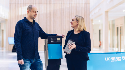 A man and a woman is talking, standing on each side of a blue industrial battery charger.