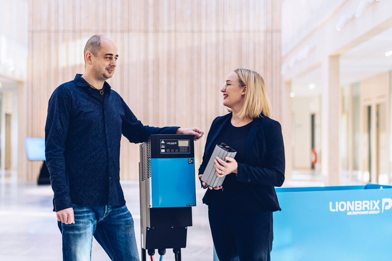 A man and a woman is talking, standing on each side of a blue industrial battery charger.